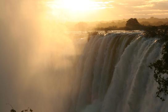 Sonnenuntergang an den Victoria Fällen in Simbabwe: Die Sonne strahlt in der aufsteiegenden Gischt